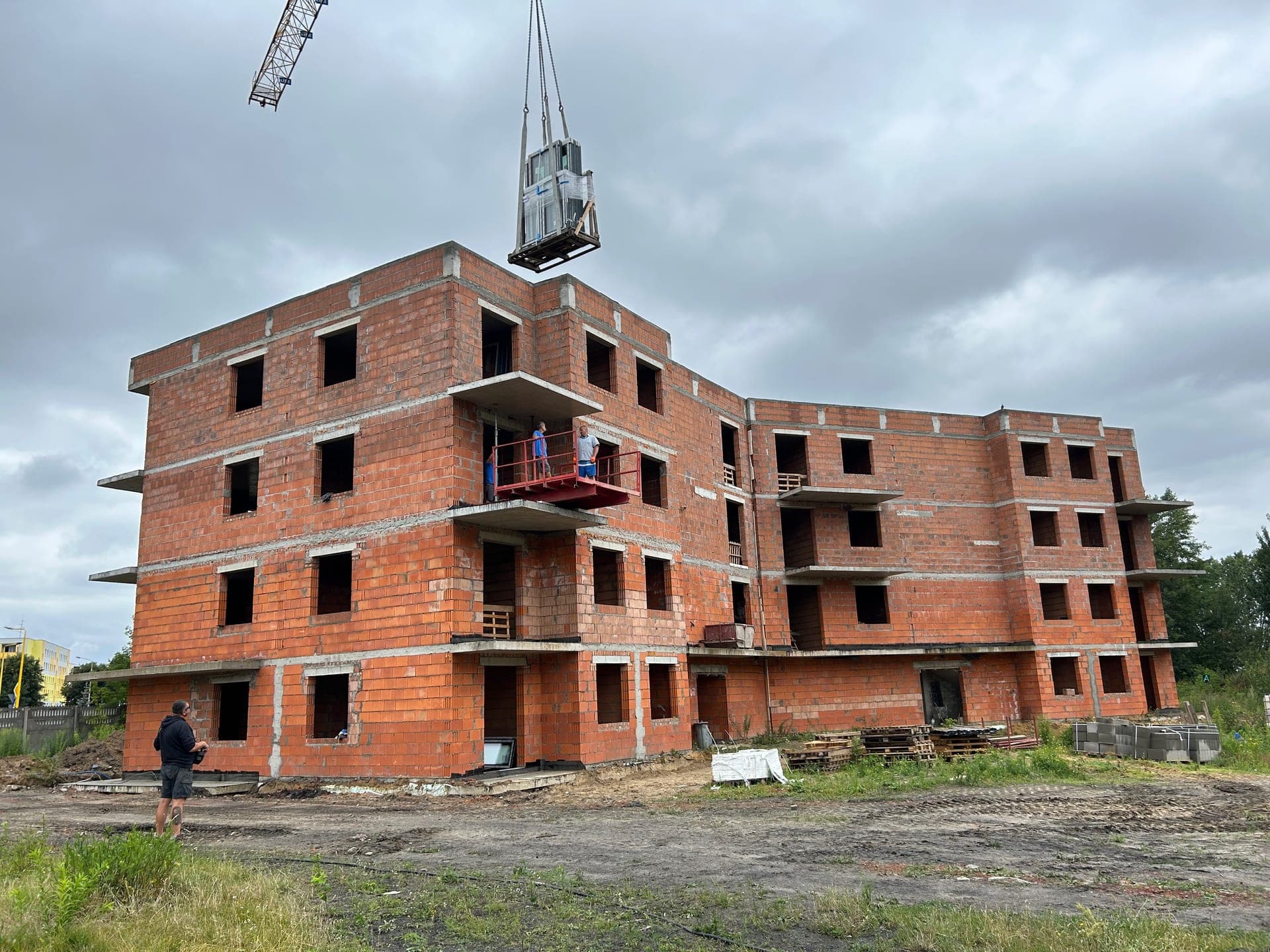 4-story apartment block under construction with crane, windows being hoisted into position